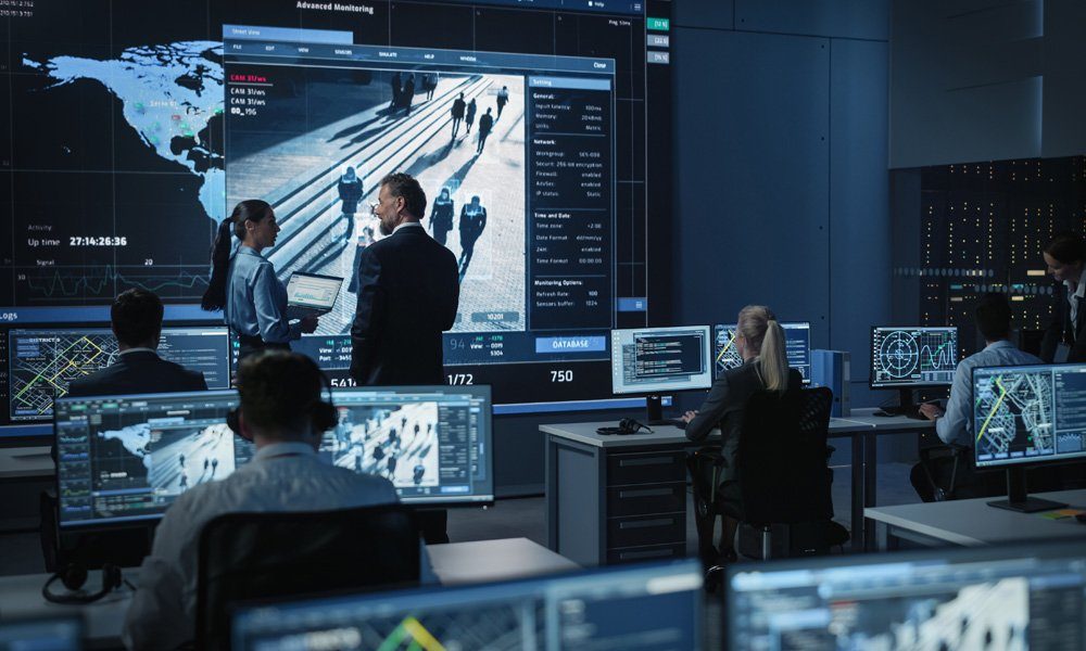 Una sala de control con varios monitores que muestran mapas, datos e imágenes de vigilancia.